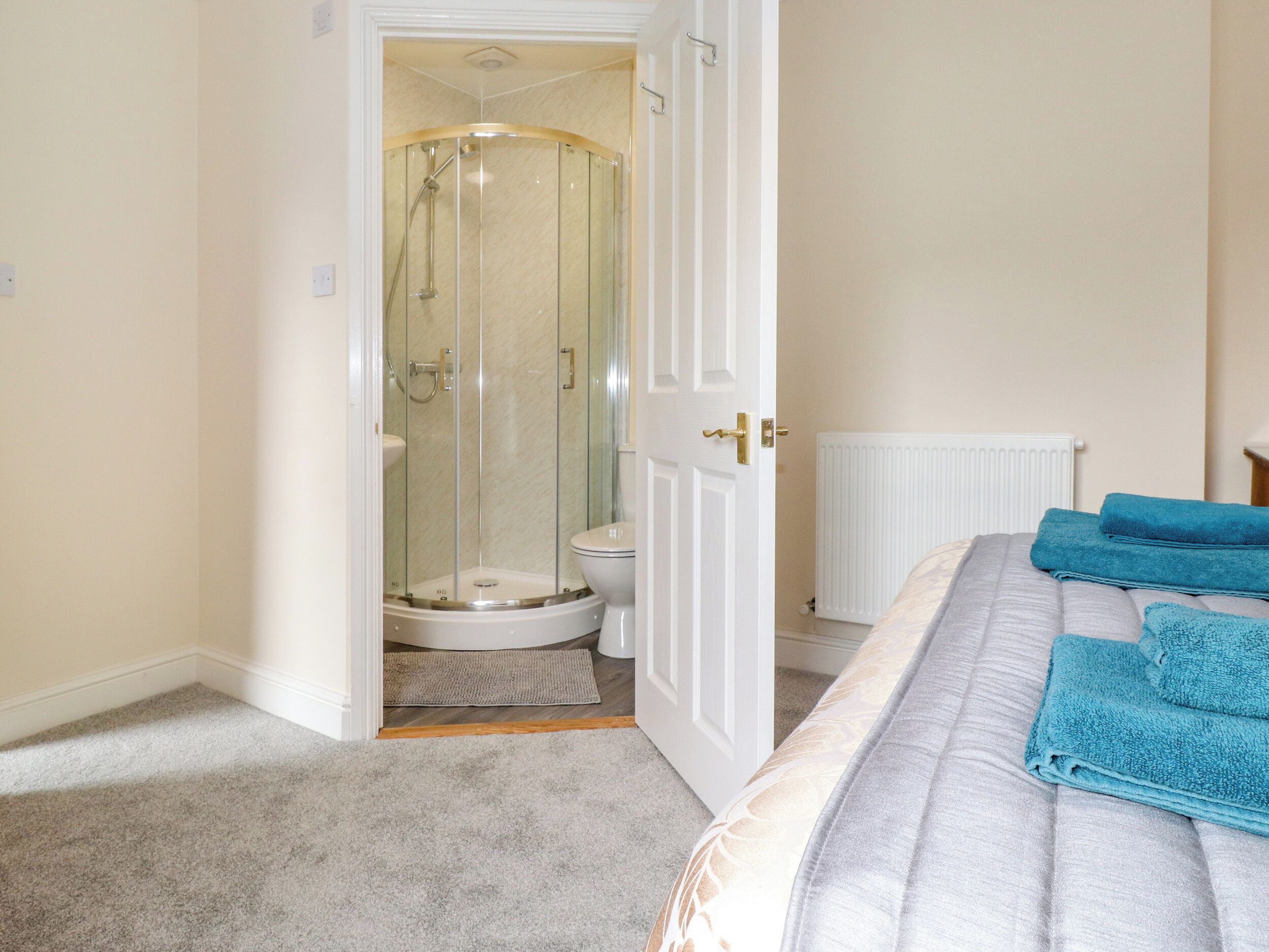 Une salle de bain avec une douche à parois de verre, des toilettes blanches et un lit avec des serviettes bleues.