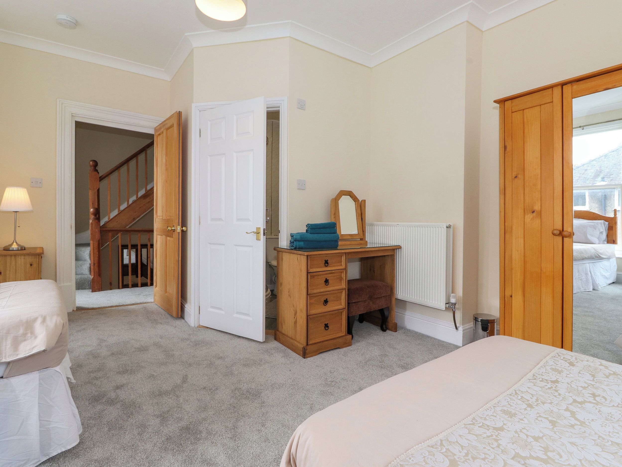 A bedroom with two beds, a wooden dresser, a mirror, and a staircase leading to another room.
