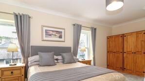 A bedroom with a bed, two bedside tables, a nightstand, a wardrobe, and a window with curtains. - Melbreak House 2 (Keswick)