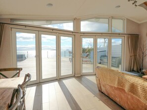 A spacious room with large sliding glass doors leading to a deck. - The Warren M45 (Pwllheli)
