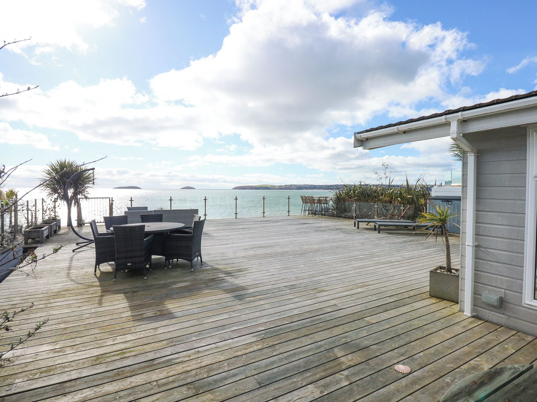 Een houten terras met buitenmeubilair, een klein gebouw en uitzicht op zee.