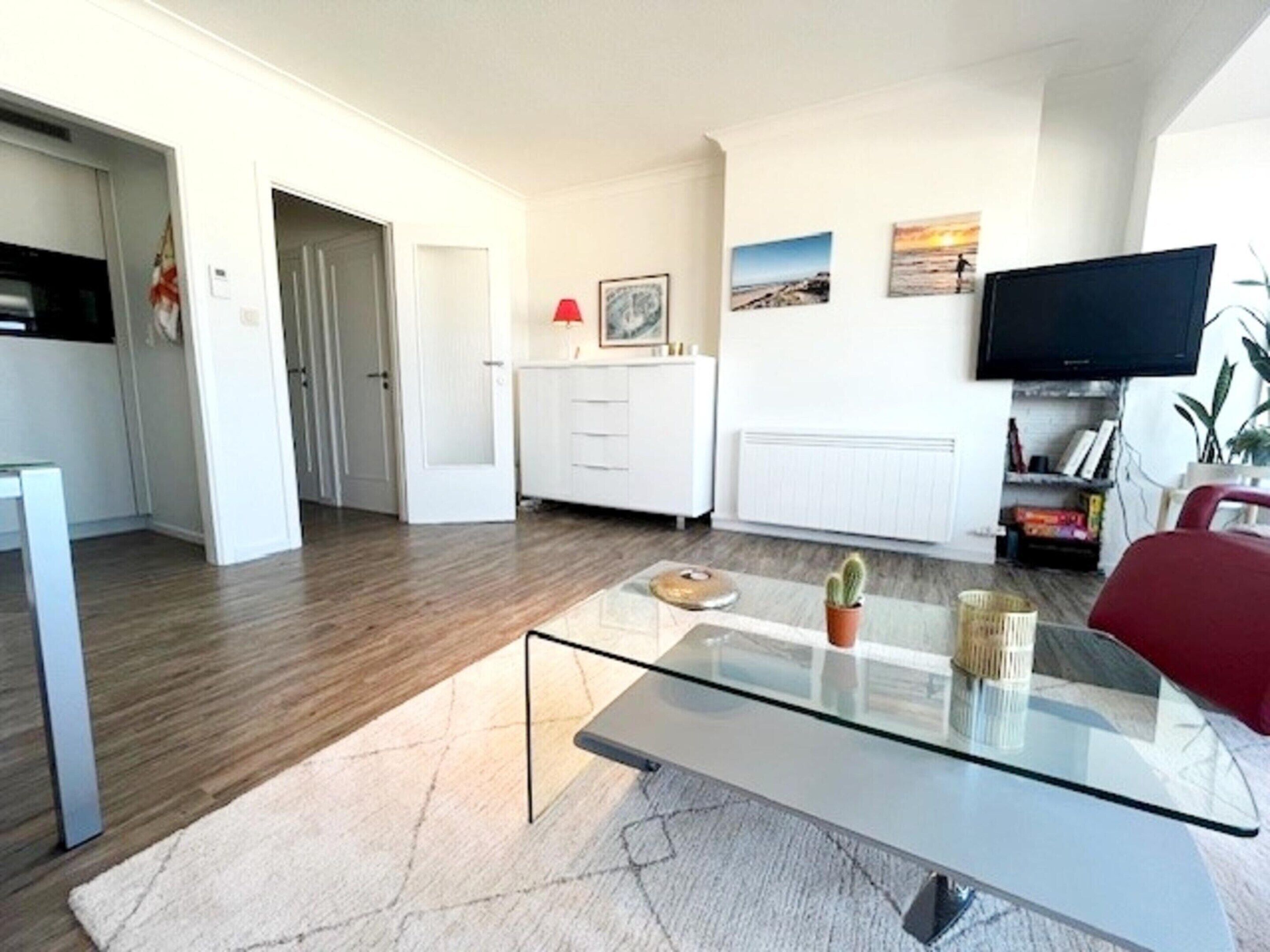 Un salon moderne avec une table basse en verre, un canapé rouge et un téléviseur à écran plat fixé au mur.