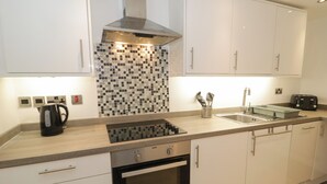 A modern kitchen with white cabinets, a stainless steel range hood, a tiled backsplash, a built-in oven, a sink, and a coffee maker. - Apartment 1 (Llandudno)