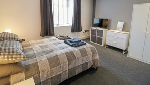 A bedroom with a bed, a TV, a wardrobe, and a window with curtains. - Apartment 1 (Llandudno)