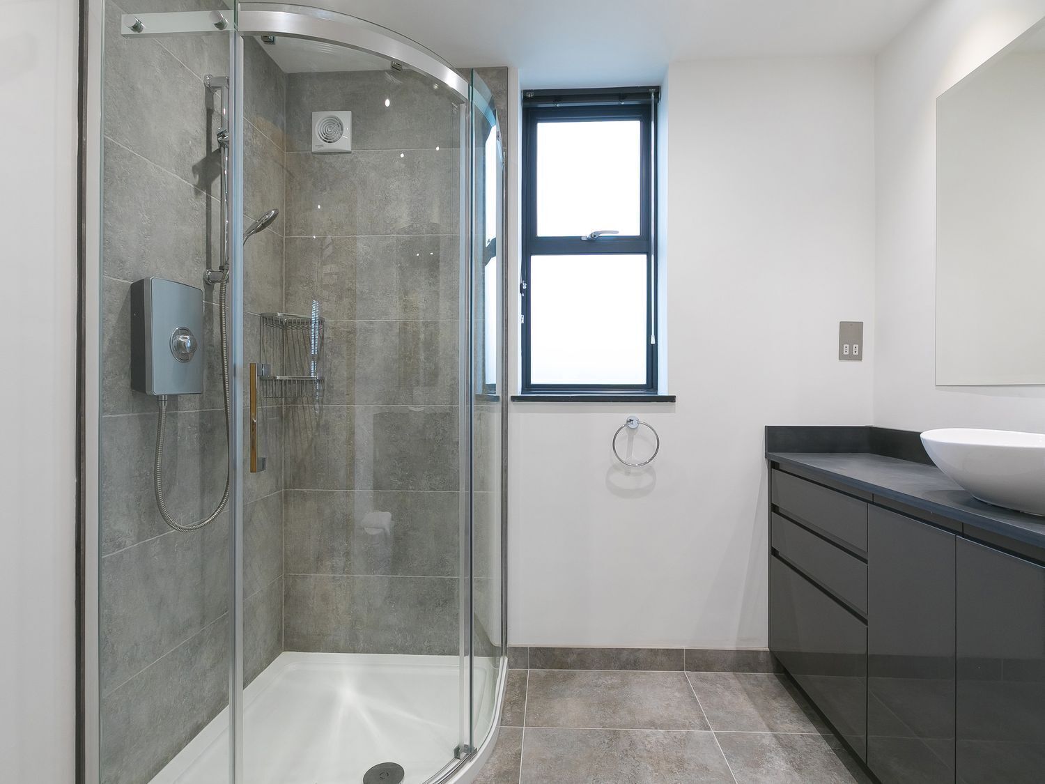 A modern bathroom with a glass-enclosed shower, a large window, and a dark-toned vanity with a bowl sink.