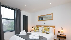 A hotel room with a large bed, two bedside tables, a mirror, and a window with curtains. - Nova Cottage (St Ives)