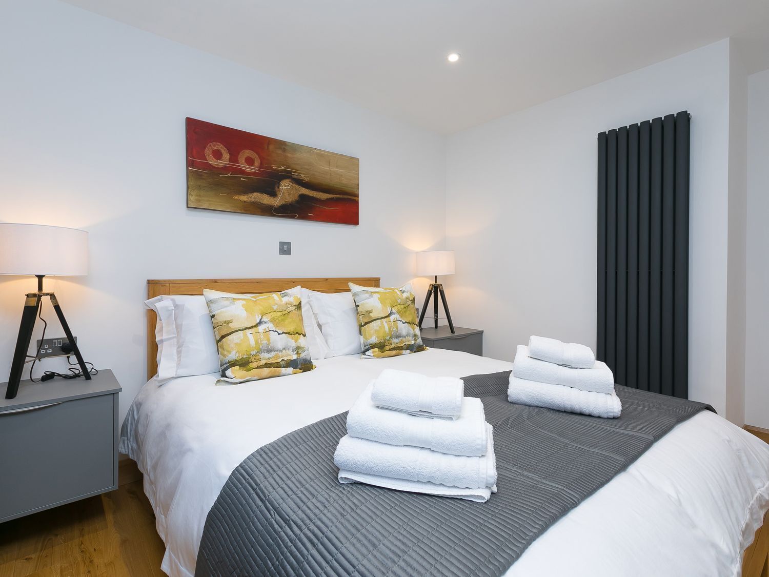 A modern hotel room with a large bed, two bedside tables, a nightstand, a painting on the wall, and a window with curtains.