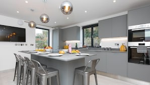 A modern kitchen with a central island, stainless steel bar stools, and a Bosch oven. - Nova Cottage (St Ives)