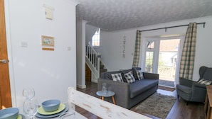 Een woonkamer met een grijze bank, een eettafel met borden en glazen, en een trap die naar een hoger niveau leidt.