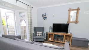 Een woonkamer met een grijze bank, een grijze fauteuil, een televisie op een houten dressoir en een bijzettafeltje met glazen.