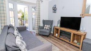 Een woonkamer met een grijze bank, een grijze fauteuil, een houten tv-meubel en een televisietoestel.
