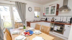 A modern kitchen with white cabinets, a stainless steel stove, and a dining area with wooden chairs and a table set for two.
