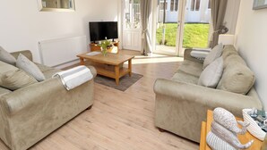 A spacious living room with two beige sofas, a wooden coffee table, and a flat-screen TV.