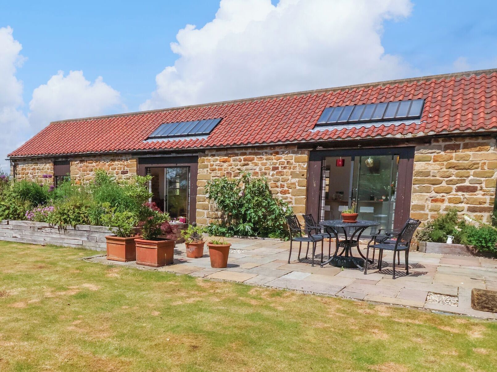 A stone building with a red-tiled roof, solar panels, and a patio with outdoor seating.