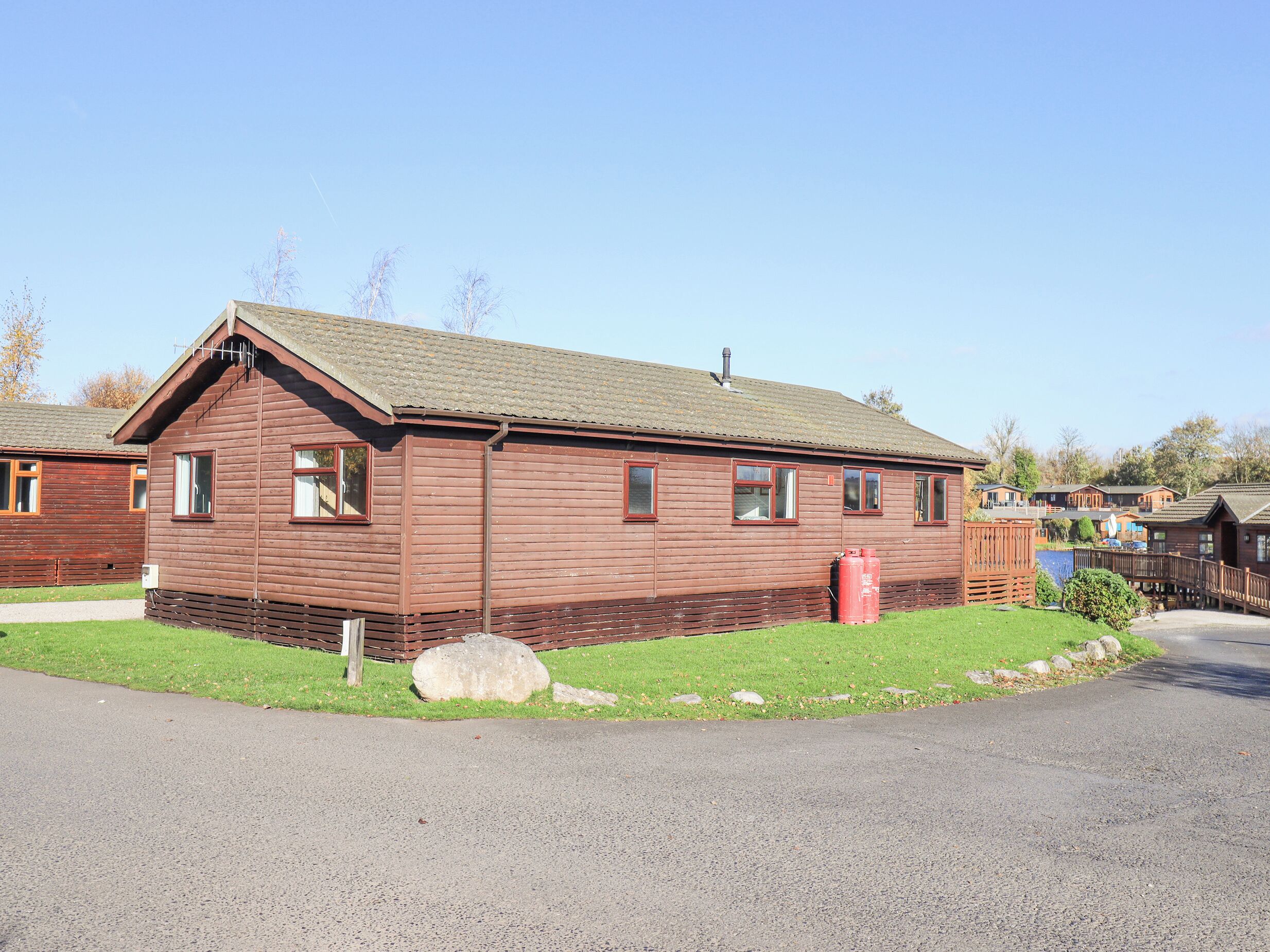 A wooden cabin with a sloped roof, a front porch, and a red barrel in the yard.