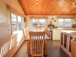 Una cocina acogedora con armarios de madera, una mesa de comedor y sillas. Hay ventanas que ofrecen luz natural y vistas al exterior.