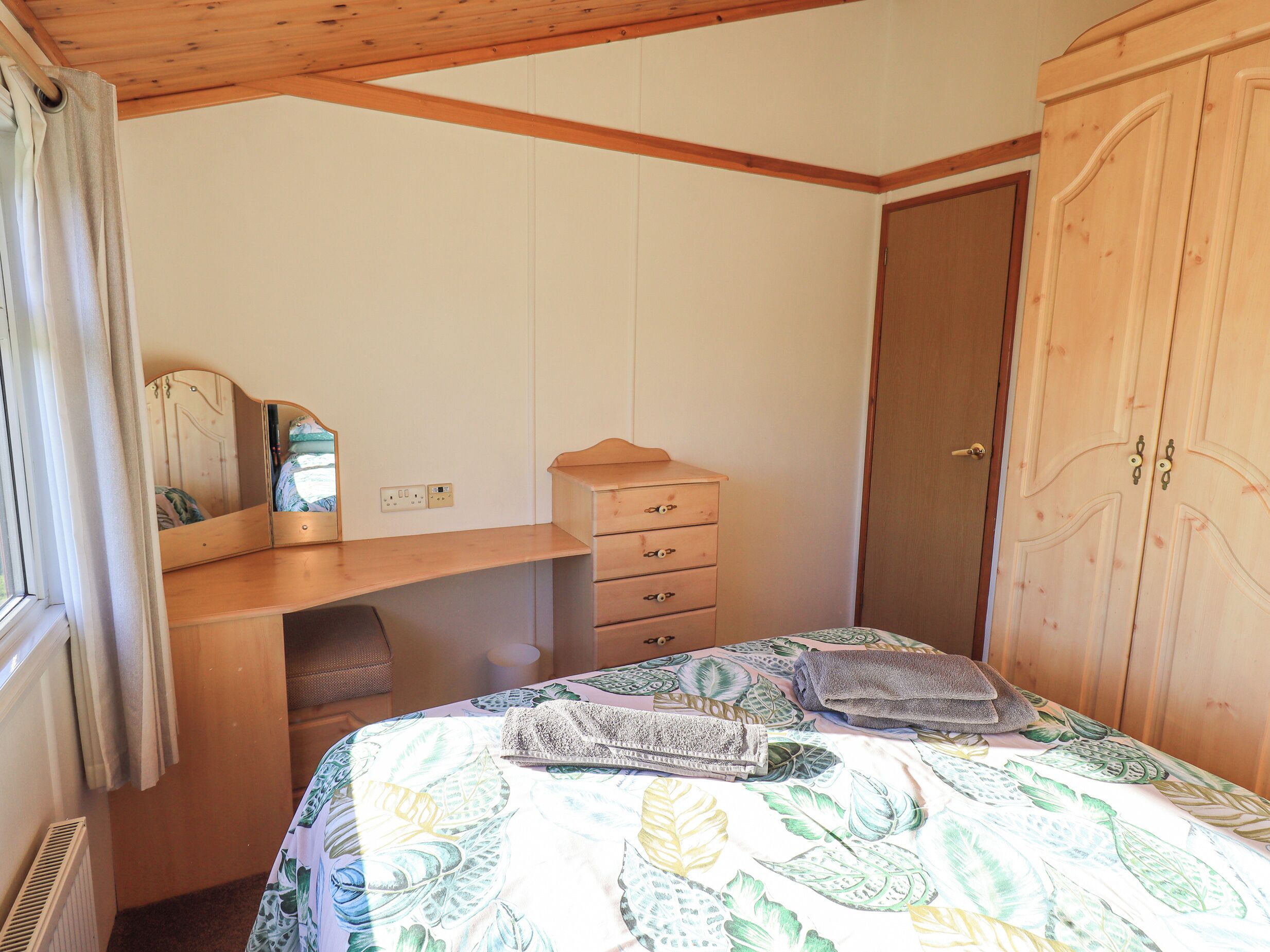 A bedroom with a bed, a wooden dresser, a mirror, and a wardrobe.