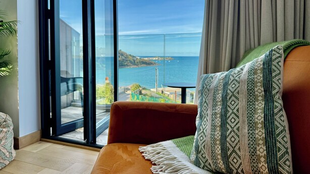 Un salon moderne doté d’une grande porte vitrée donnant sur un balcon avec vue sur la mer.