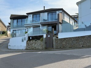 A modern two-story house with a stone wall and a glass balcony. - Bayvista (St Ives)