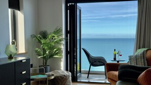 Un salon moderne avec vue sur la mer, un coin repas avec une table et des chaises, et une grande plante en pot.