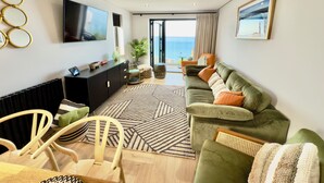 Un salon moderne avec un canapé, des fauteuils, un téléviseur et une vue sur la mer grâce à de grandes fenêtres.