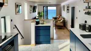 Une cuisine moderne dotée d’un îlot central, un coin repas avec vue et un espace de vie comprenant un canapé et une plante.