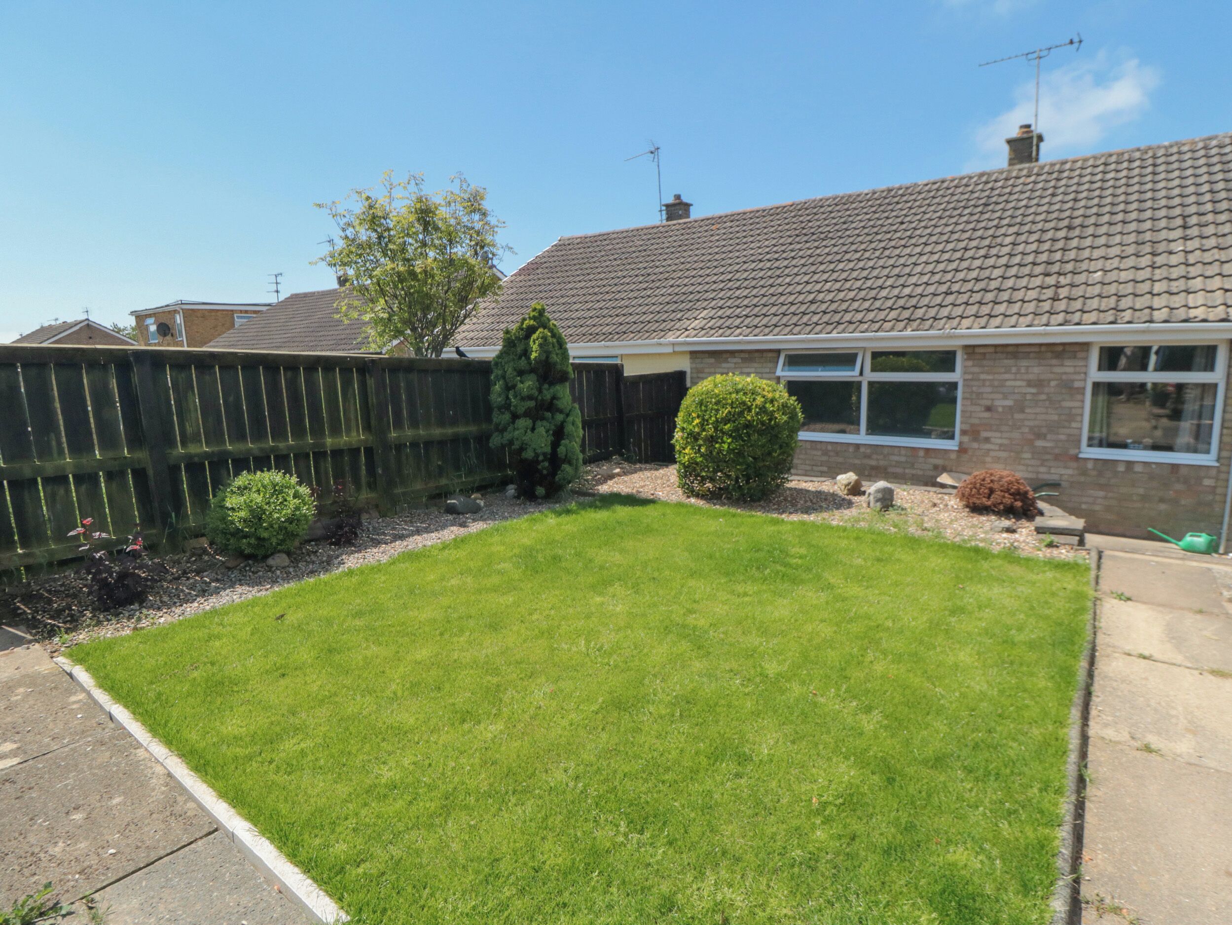 A residential property with a well-maintained lawn, a wooden fence, and a brick house with a tiled roof.