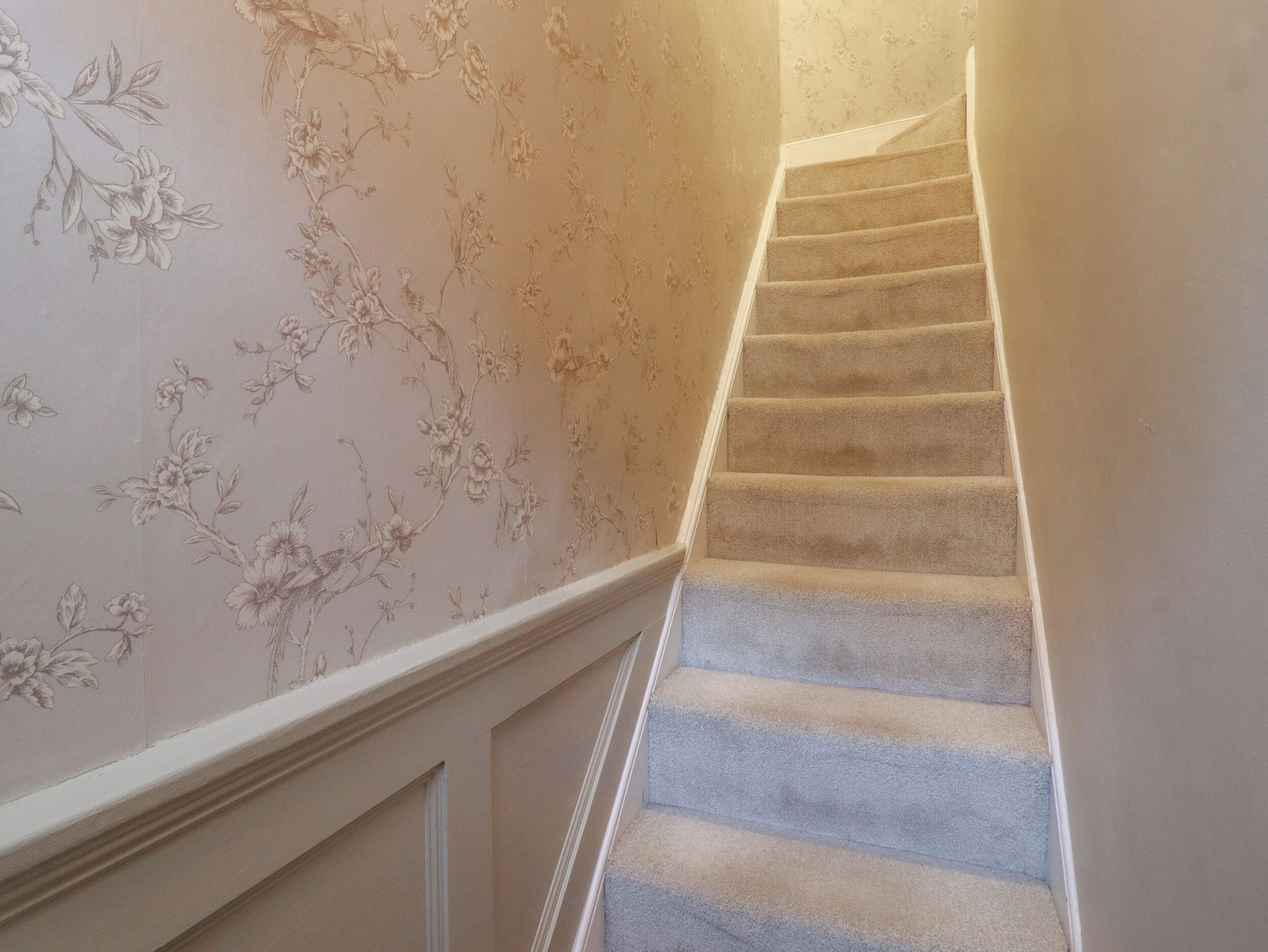 A carpeted staircase with floral wallpaper on the walls.