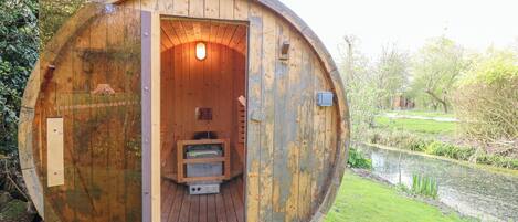 Een houten, vatvormig gebouw met een openstaande deur, die een klein interieur onthult met treden naar een platform.