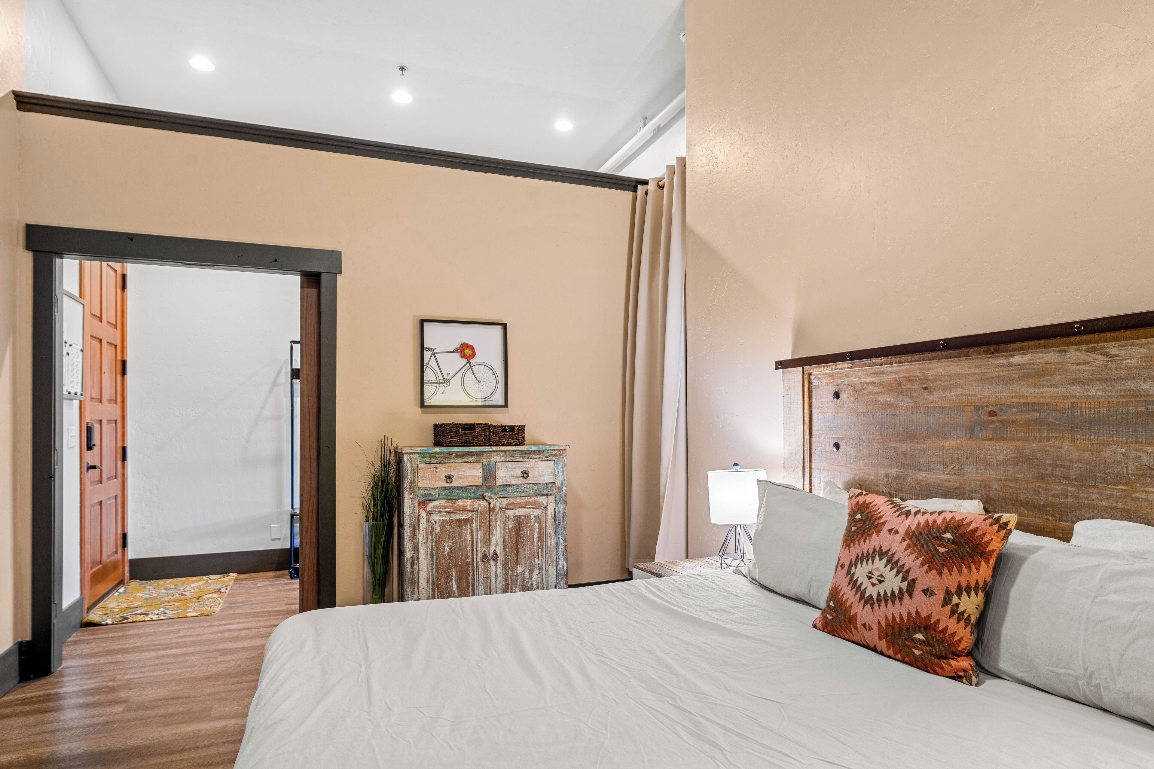 A bedroom with a large bed, a wooden headboard, a small dresser, and a framed picture on the wall.