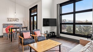 A spacious living room with a large window, a flat-screen TV, and a 'LOVE' wall art piece. - Loft on Main St, Access to All Mountain Activities (Frisco)