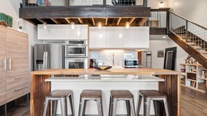 A modern kitchen with a central island, bar stools, stainless steel appliances, and a staircase leading to an upper level. - Loft on Main St, Access to All Mountain Activities (Frisco)