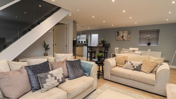 A modern living room with two sofas, a staircase, a dining area, and a kitchen in the background. - The Bungalow at 46 Church St (Chorley)