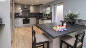 A modern kitchen with grey cabinets, a black countertop, and a wooden floor. There are two chairs at the island, and a vase with flowers on the countertop. - The Bungalow at 46 Church St (Chorley)