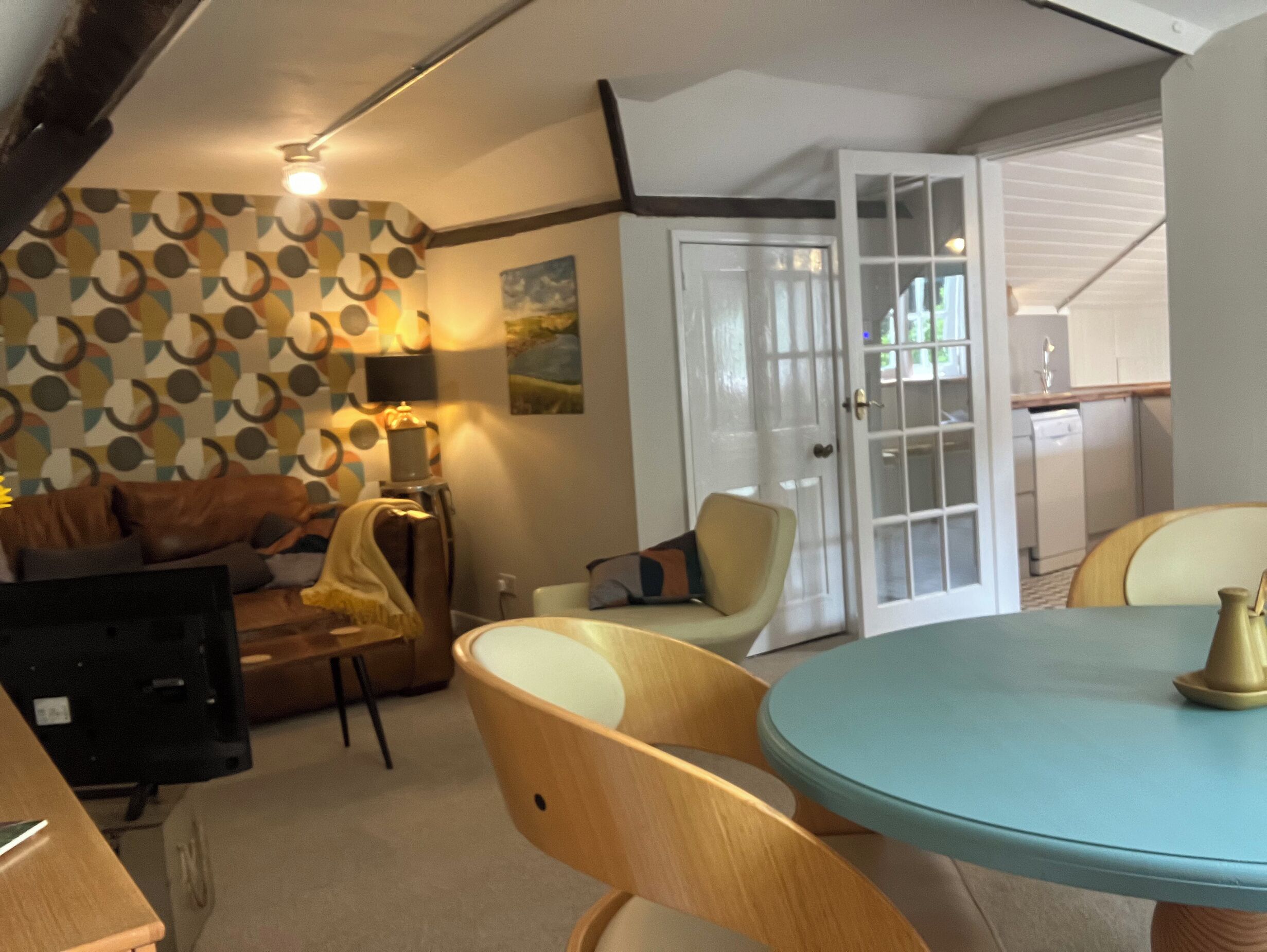 Una sala de estar acogedora con un papel tapiz estampado, un sofá, una mesa de centro y una mesa de comedor con sillas.
