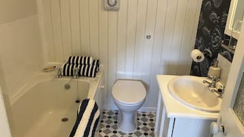 Ett badrum med badkar, toalett och handfat. Det ligger ett randigt handduk på badkarskanten och golvet har ett mönster.