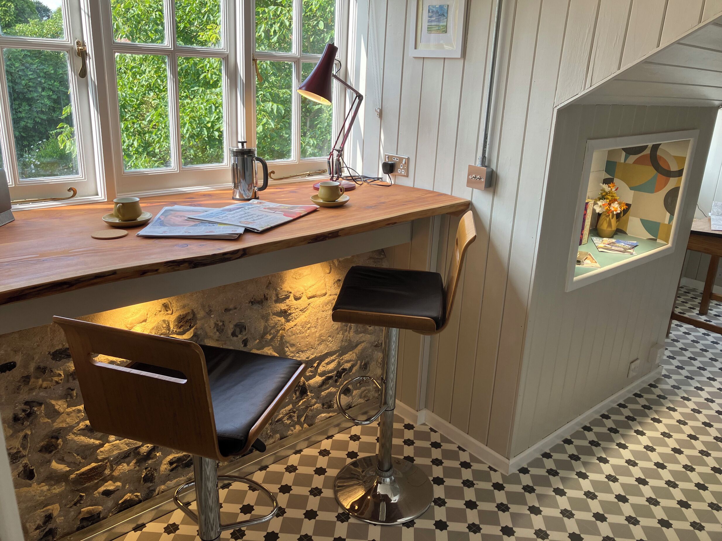 Una cocina acogedora con encimera de madera, cafetera y hervidor. Hay dos taburetes altos y una ventana con vistas a zonas verdes.