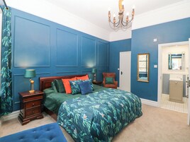 A bedroom with a large bed, a nightstand, a chair, a dresser, a mirror, and a chandelier.