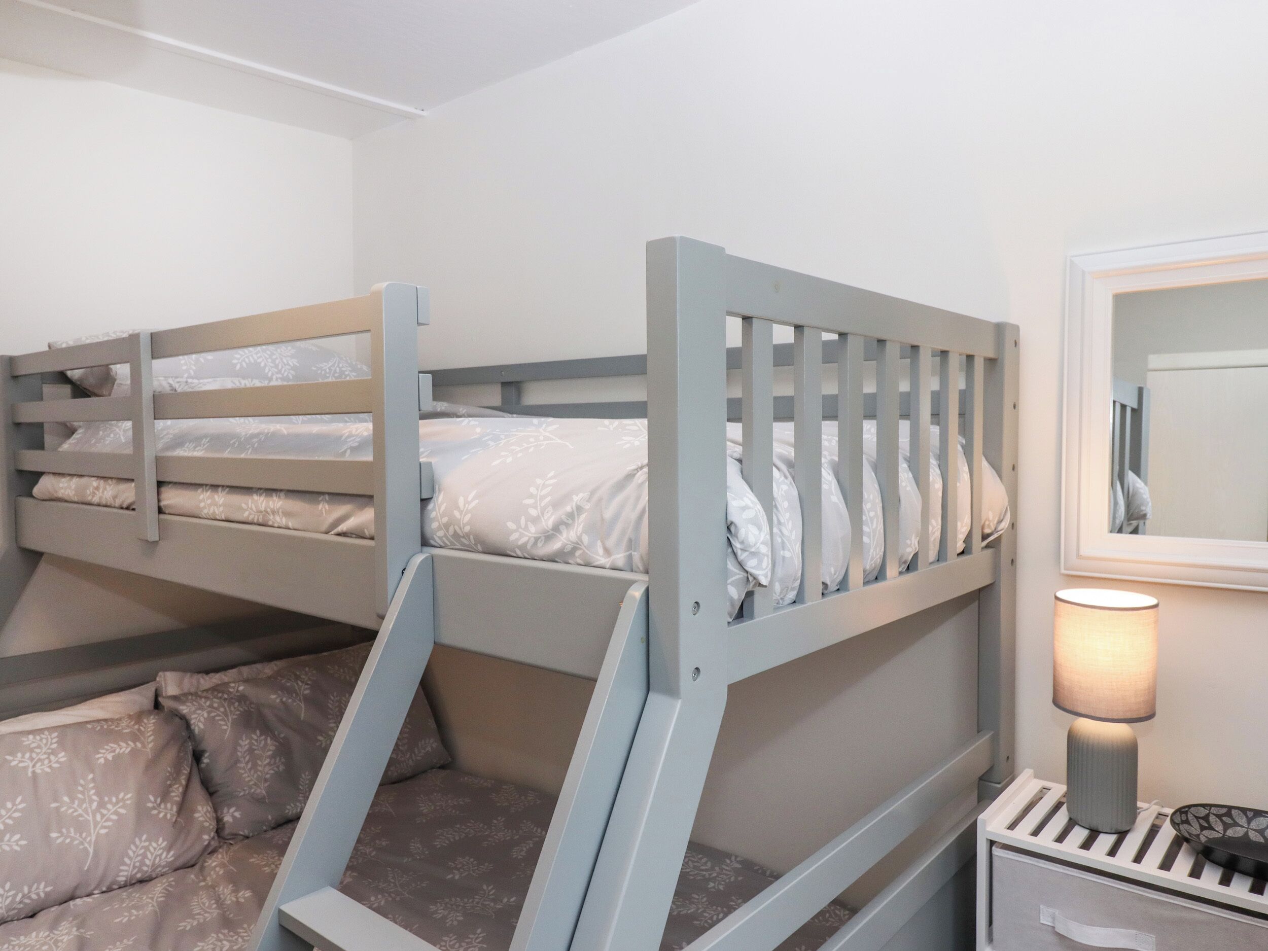 Un lit superposé avec une tête de lit, une table de chevet avec une lampe et un miroir.