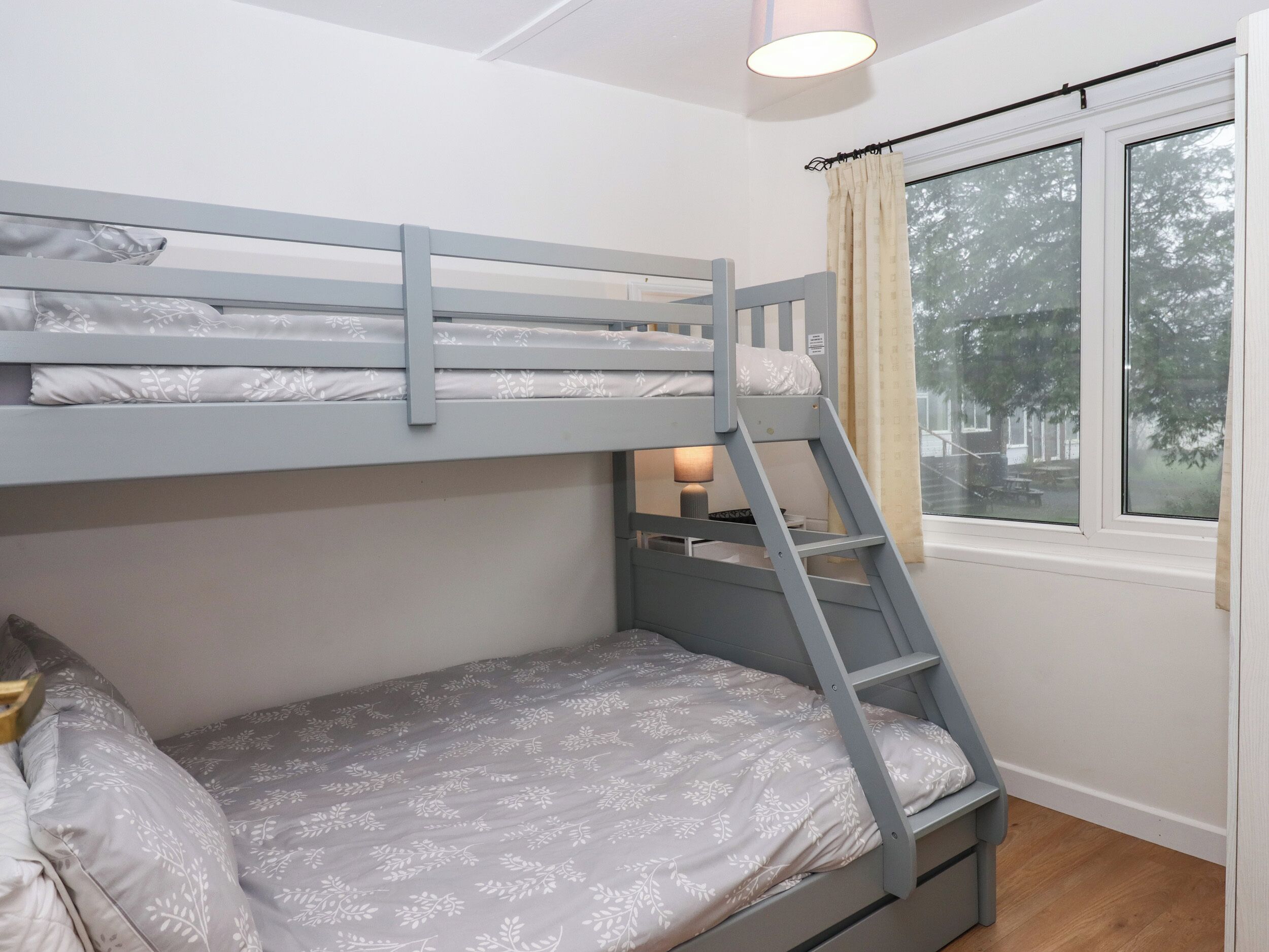 A bunk bed with a ladder, a bedside table with a lamp, and a window with curtains.