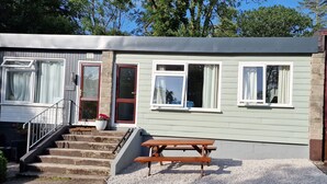 A two-story building with a front entrance, a staircase, and a picnic table. - 2 The Glade (Bude)