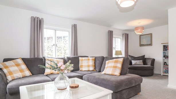 A modern living room with a grey sectional sofa, a glass coffee table, and a bookshelf. - One Side House Farm (Ambleside)