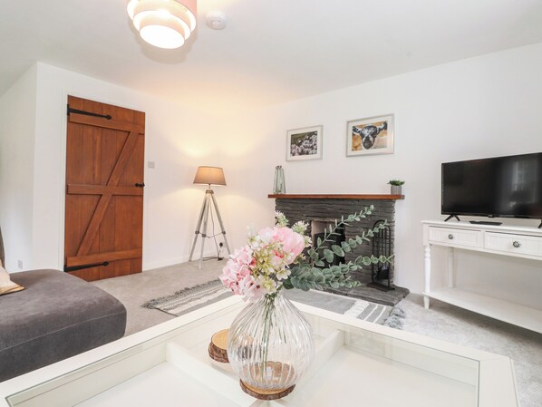 A living room with a fireplace, a television, and a coffee table with a vase of flowers.