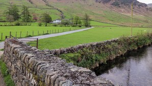 A stone wall beside a calm stream, a grassy field, and a house in the background. - One Side House Farm (Ambleside)