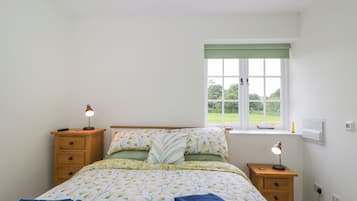 Une chambre à coucher comprenant un lit, deux tables de chevet, une fenêtre donnant sur un espace verdoyant et une prise électrique.