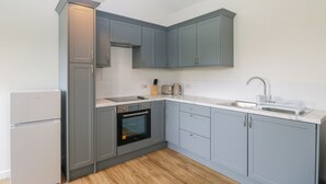 A modern kitchen with grey cabinets, a built-in oven, a sink, and a pendant light. - Sunset Cottage (Towcester)