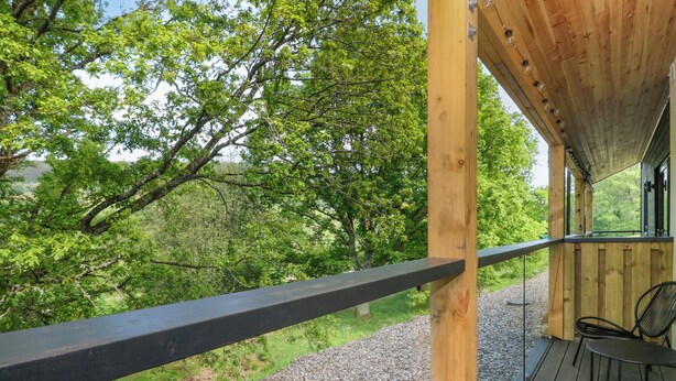 Un pontile in legno con ringhiera metallica che si affaccia su un vialetto sterrato e vegetazione rigogliosa.