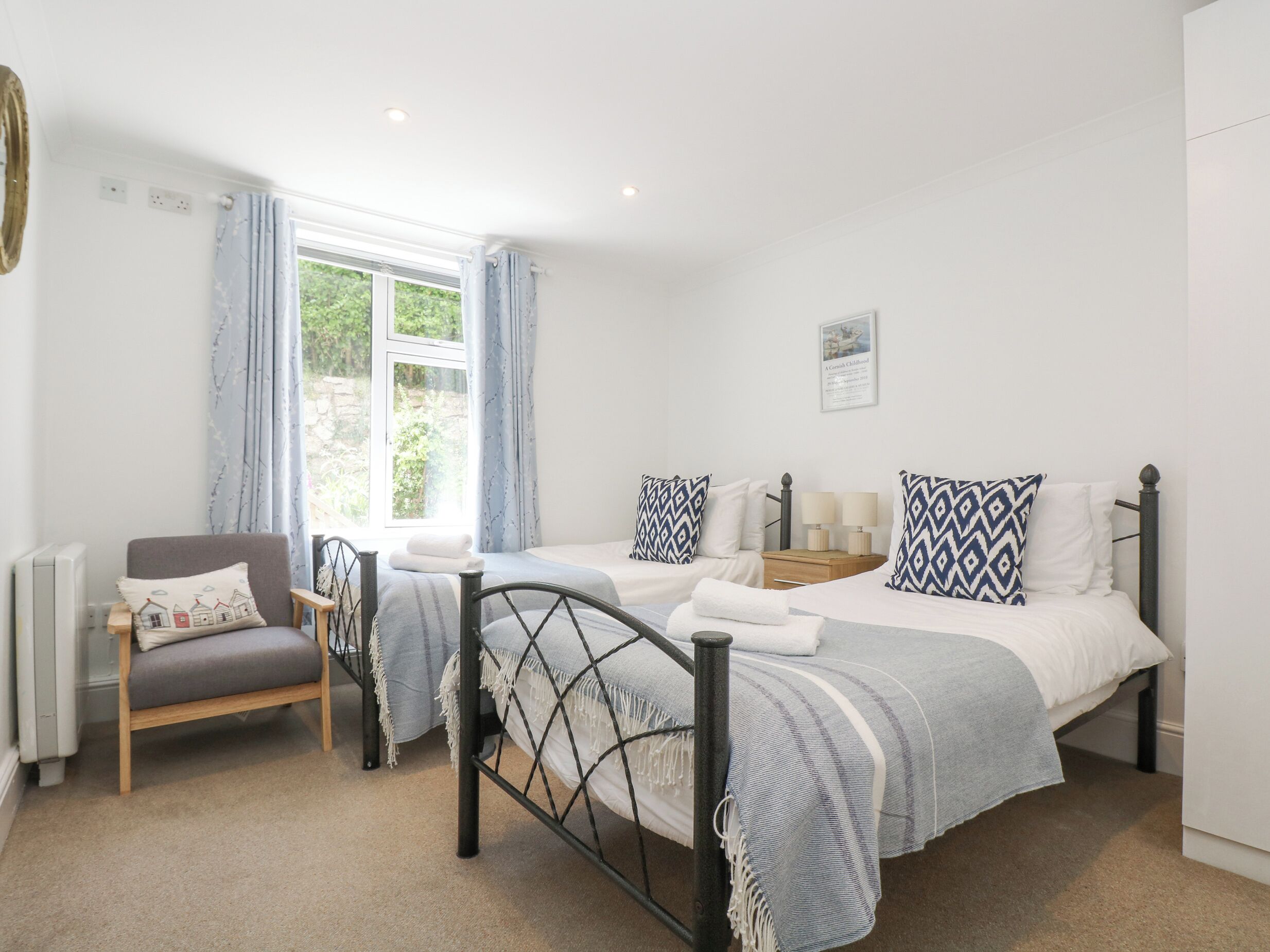 A bedroom with two beds, a chair, a window, and a radiator.