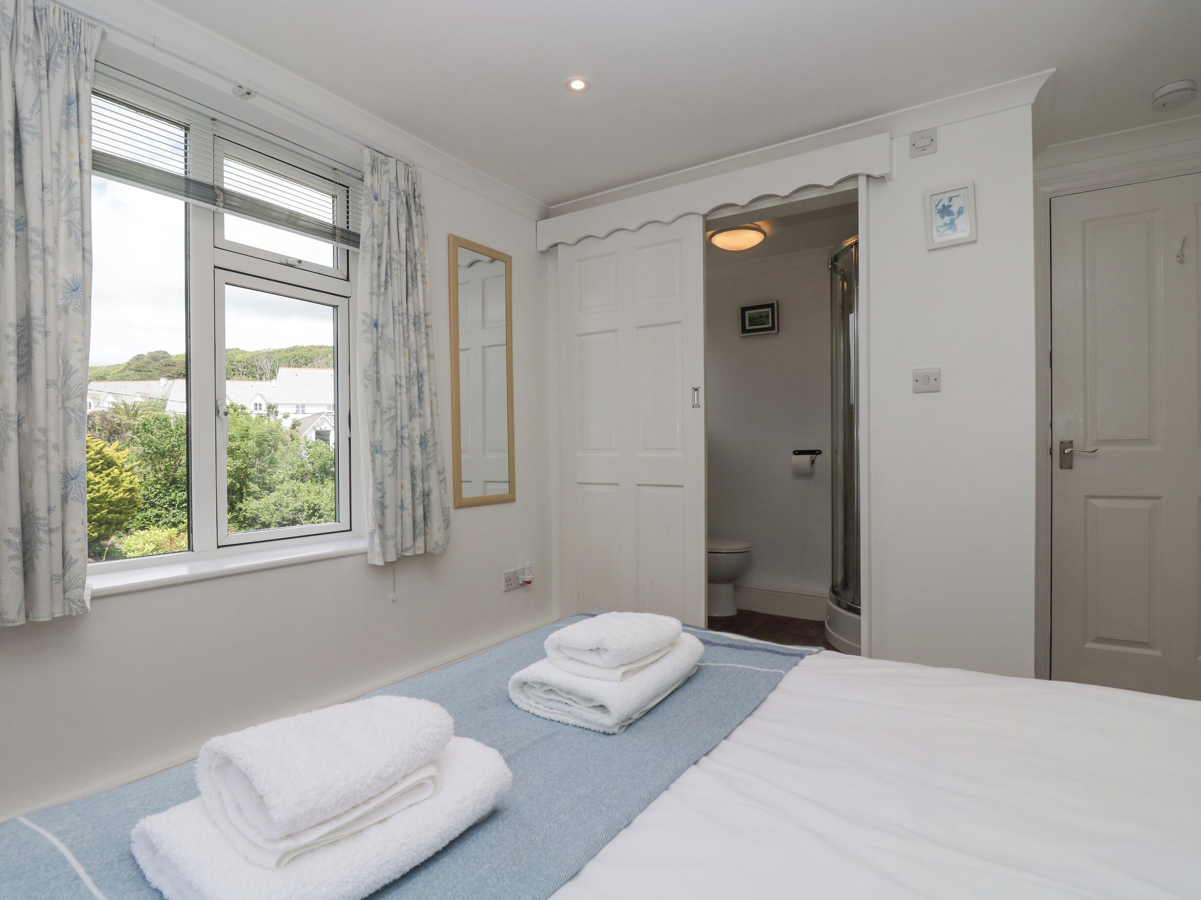 A bedroom with a bed, two towels, a window with curtains, a mirror, and a door leading to a bathroom.