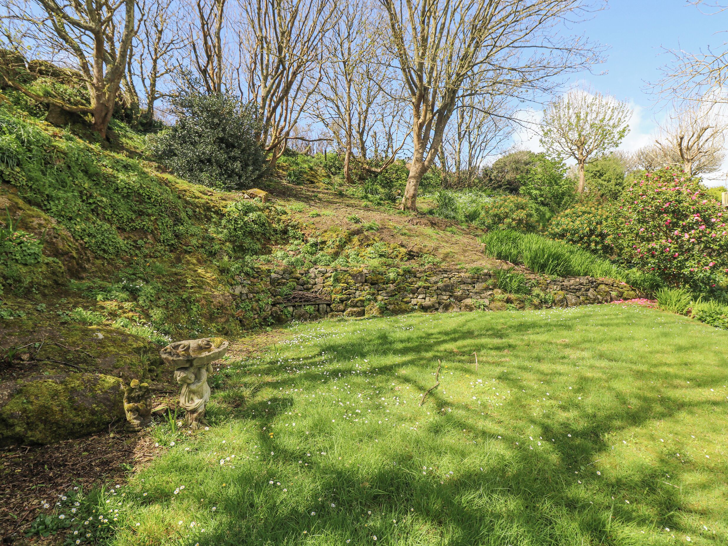 A lush garden with a stone wall, a statue, and various plants.